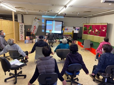 モニター前に座っている橋本明先生の真似をして両手を広げている参加者を後方から写した写真