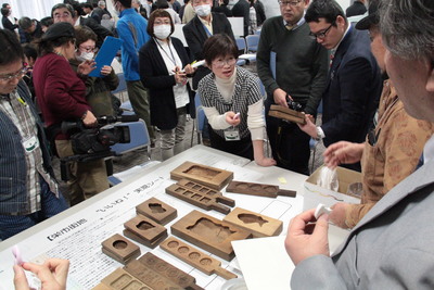 丸や四角、魚の形などをした木製の型が置かれた机の周りに集まった参加者が話し合っているワークショップの様子の写真
