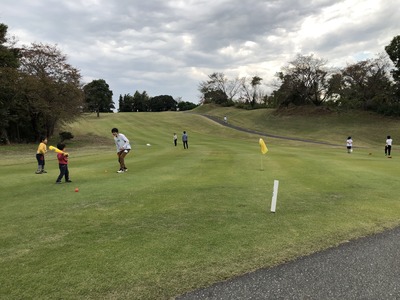平坦なゴルフコースで間隔をあけてボールで遊んでいる親子連れなどの写真