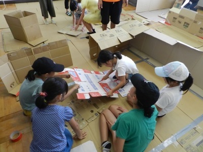 女子児童5人が協力しながら災害時用の段ボールハウスを作っている様子の写真