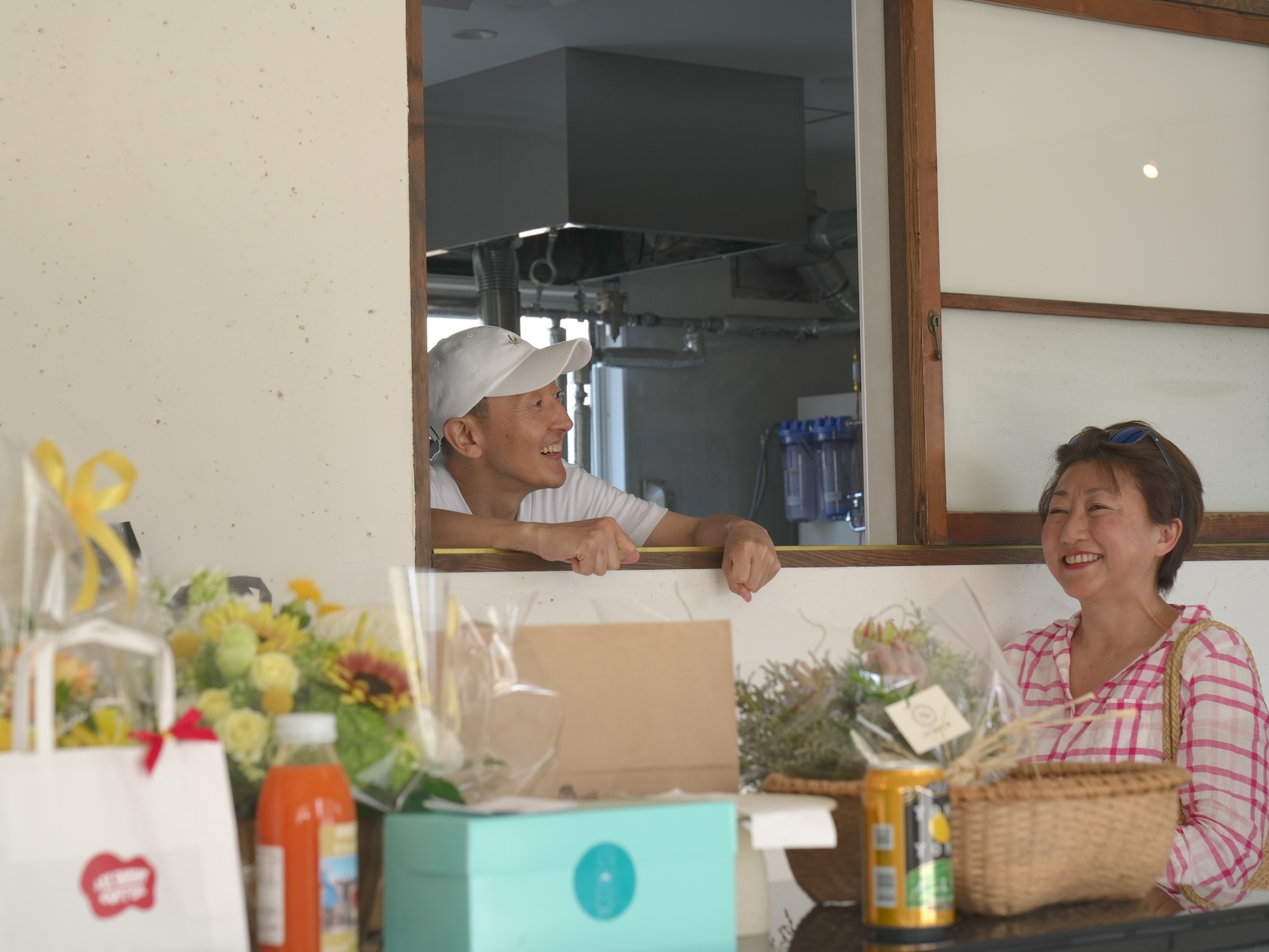 豆腐をつくる工房と店の間の窓越しに談笑する金原さんの写真