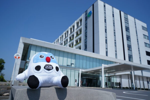 フックン船長がつくば市役所本庁舎を見上げている様子