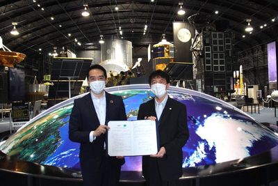 JAXAの施設内で寺田筑波宇宙センター所長と協定書を持ち記念撮影するつくば市長の写真