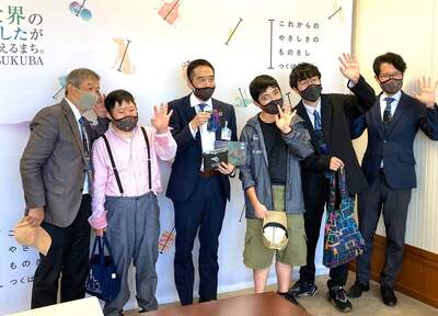 （集合写真）自然生クラブと坂本さん、市長、毛塚副市長が手のひらを顔の横に掲げて立っている様子