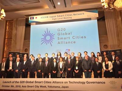 プロジェクターで映し出された大きな画面の前で記念撮影をしている人達の写真。画面には「G20 Global Smart Cities Aliance」と書かれている。