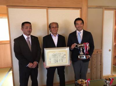 鳩レース表彰式での賞状を持っている竹井会長とトロフィーを持っている五十嵐市長の写真