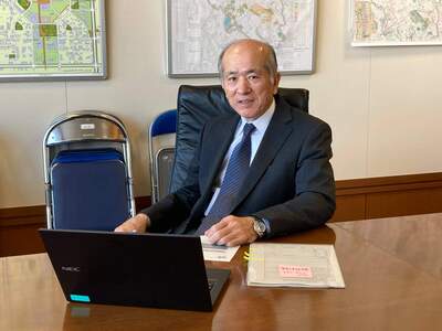 椅子に腰かけている黒のスーツを着た飯野副市長の写真