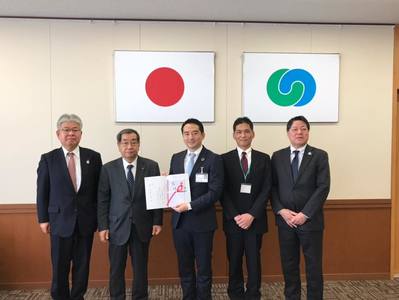 背景に日本の国旗とつくば市の市章があり、4名の寄贈者と市長が並んでいる写真