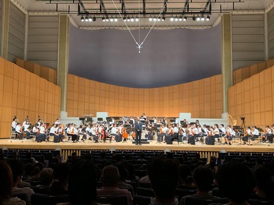 ステージの上で楽器を演奏するオーケストラの方々を撮影した写真。