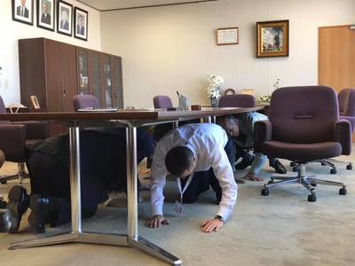 市長を含む複数の方が机の下に隠れているシェイクアウト訓練の写真