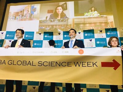 市長が他の登壇者と壇上で並び立ち、「TSUKUBA GLOBAL SCIENCE WEEK」と印字された横断幕を持っている様子
