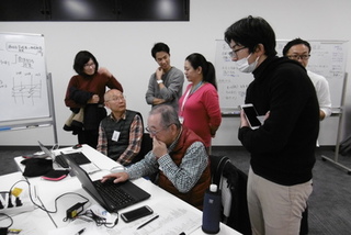 ノートパソコンを操作している人の傍に集まって話し合いをしているグループの写真