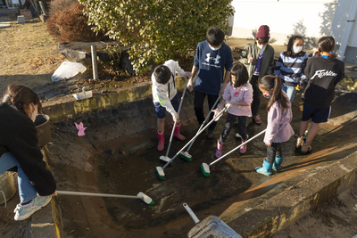 水を抜いた池の底を掃除する子供たちの写真