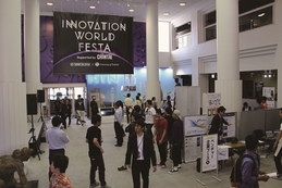 「INNOVATION WORLD FESTA」と書かれた黒い幕の飾られたホールに多くの人が集まっている写真