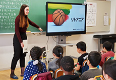 女性がモニターに映るバスケットボールと「リトアニア」の文字を指さしながら子供たちに話している写真