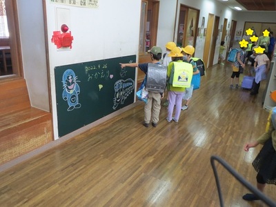 絵とおかえりの言葉が添えられた児童館の廊下の大きな黒板とそれを見ている子どもたちの写真
