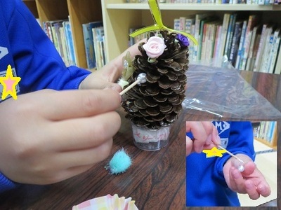 松ぼっくりに花やパールなどの装飾をしている様子の写真