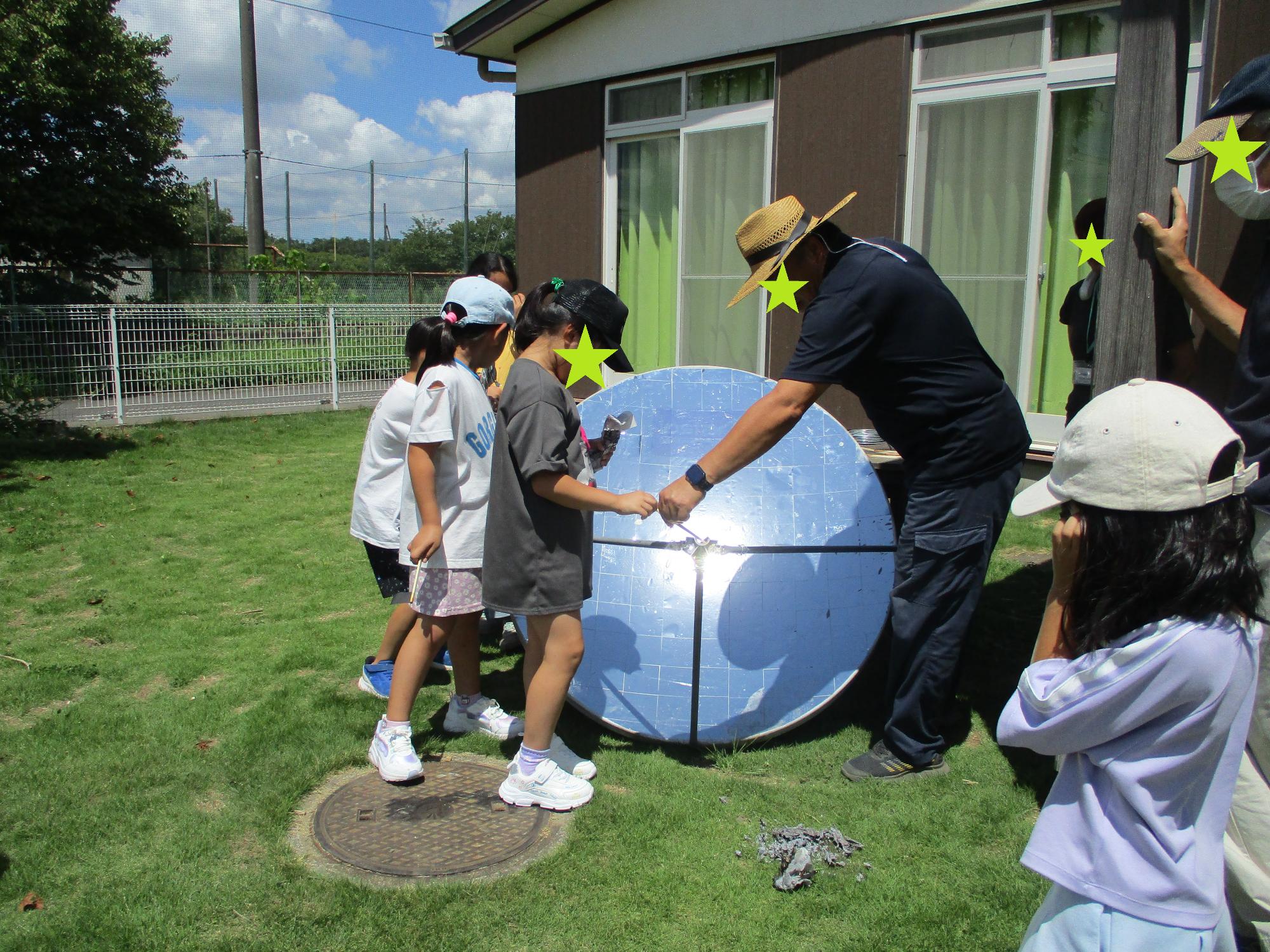 太陽光で火おこしに挑戦する子どもたちと館長