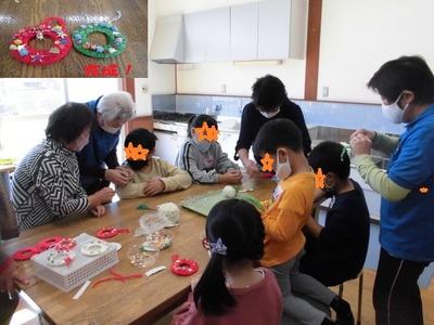 大人と一緒に子供たちが赤や緑のクリスマスリースを作っている様子の写真