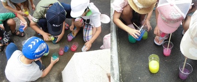 子どもたちがプラスチックのコップに色水を入れている写真