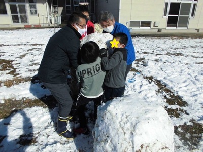 先生たちと一緒に雪の塊を持ち上げている様子の写真