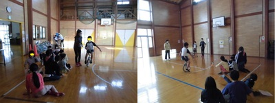 体育館で子どもが一輪車に乗っている様子とそれを見ている他の先生と子どもたちの様子。