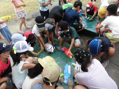 子どもたちが大きな水槽から水鉄砲に入れる水をすくっている写真