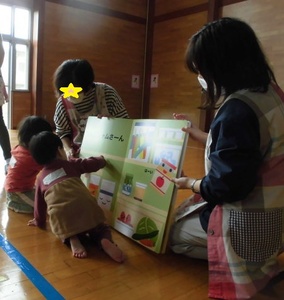 子どもが座った状態よりも大きな絵本を読む子どもたちの写真