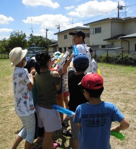 子どもたちが一人の大人に水鉄砲を向けている写真