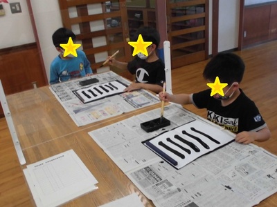子どもたちが書道で筆で紙に一の漢字を書いている様子の写真