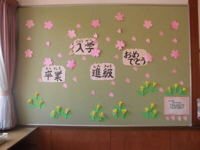 壁に紙でできた桜やタンポポ「卒業」「入学」「進級」「おめでとう」と書かれたメッセージが飾られた写真