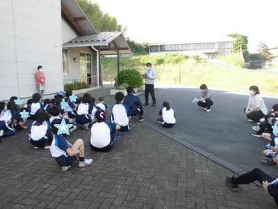 建物の外で集まり、先生の話を聞く子供たちの写真