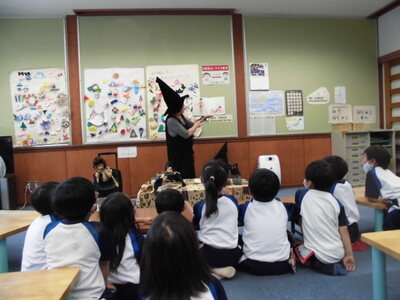魔女の格好をした先生が、子どもたちに絵本を読み聞かせている様子