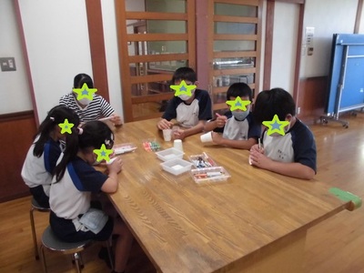 子供たちがテーブルの上で紙コップに絵を描いたり、マジックになるカードを作成している様子の写真