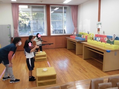 2名の女の子が壁側に設置された的に向けてが空気銃を構えている射的ゲームの様子の写真