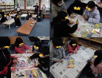 新聞を敷いた机を囲みペンでカラフルに色づけた凧を作る子供たちの写真