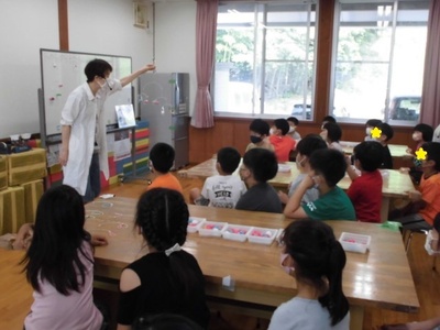 白衣を着た先生が子どもたちに実験の方法について説明している写真