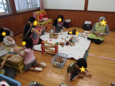 エプロンを着用したボランティアの方たちと一緒におもちゃなどで遊んでいる子供たちの写真