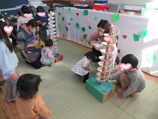 どんぐりころがしゲームで小さな子にやさしく遊ばせている年長児の様子