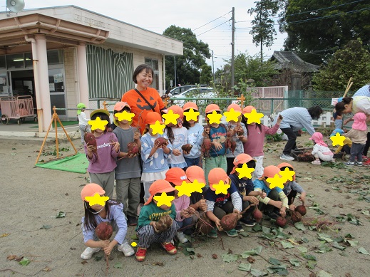 収穫した芋を持ち記念写真をとるすみれ組