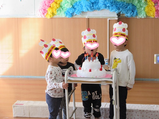大きな誕生日ケーキのロウソクを吹き消そうとする子どもたち