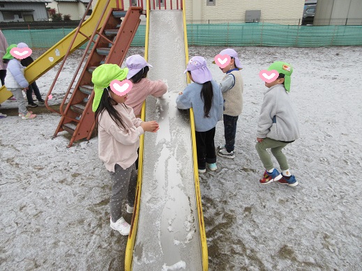 滑り台に積もった雪で遊ぶ子どもたち