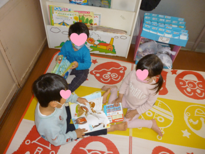 子ども三人が座りながら絵本を開いて読んでいる写真