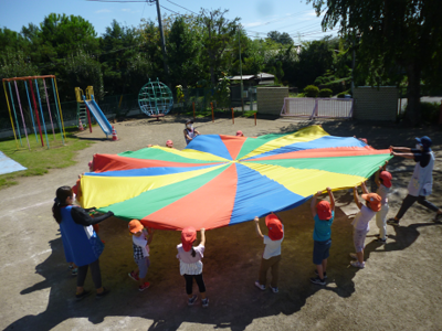 放射状に広がるカラフルな色の布を円になって広げる先生と園児たちの写真