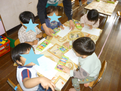 子どもたちがテーブルに座りクレヨンで絵を描いている写真