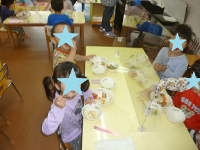 子どもたちがパーテーションで区切られた机で給食を食べながらカメラに顔を向けている写真