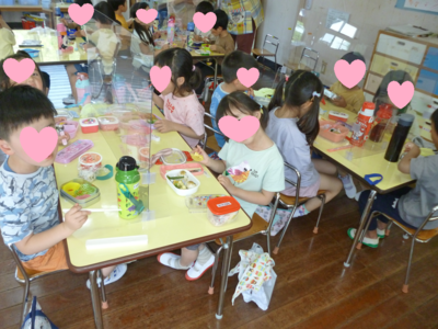子どもたちがテーブルに座ってお弁当を食べたりカメラに顔を向けている写真