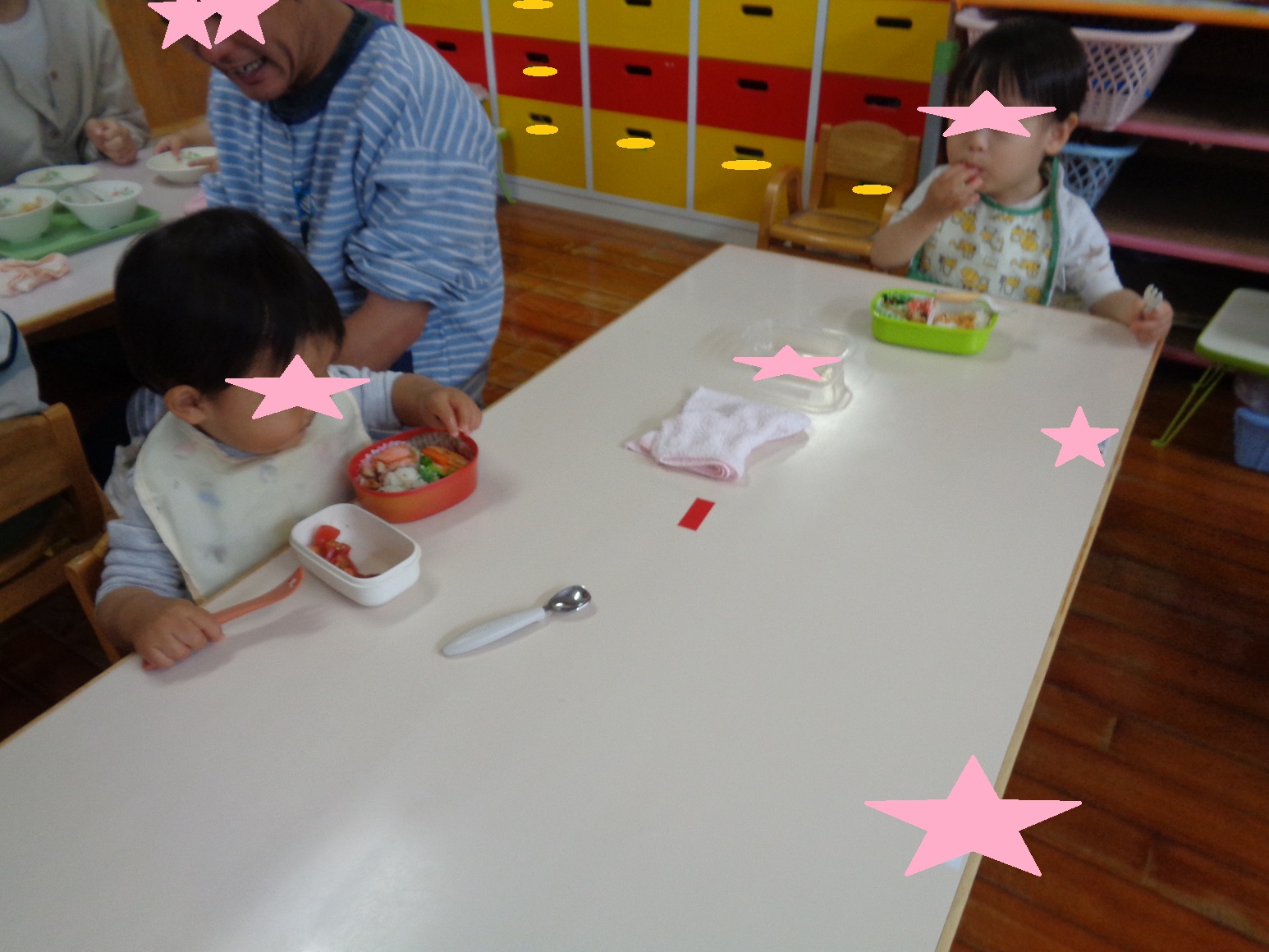椅子に座りお弁当箱の中の食べ物に手を伸ばしている子ども