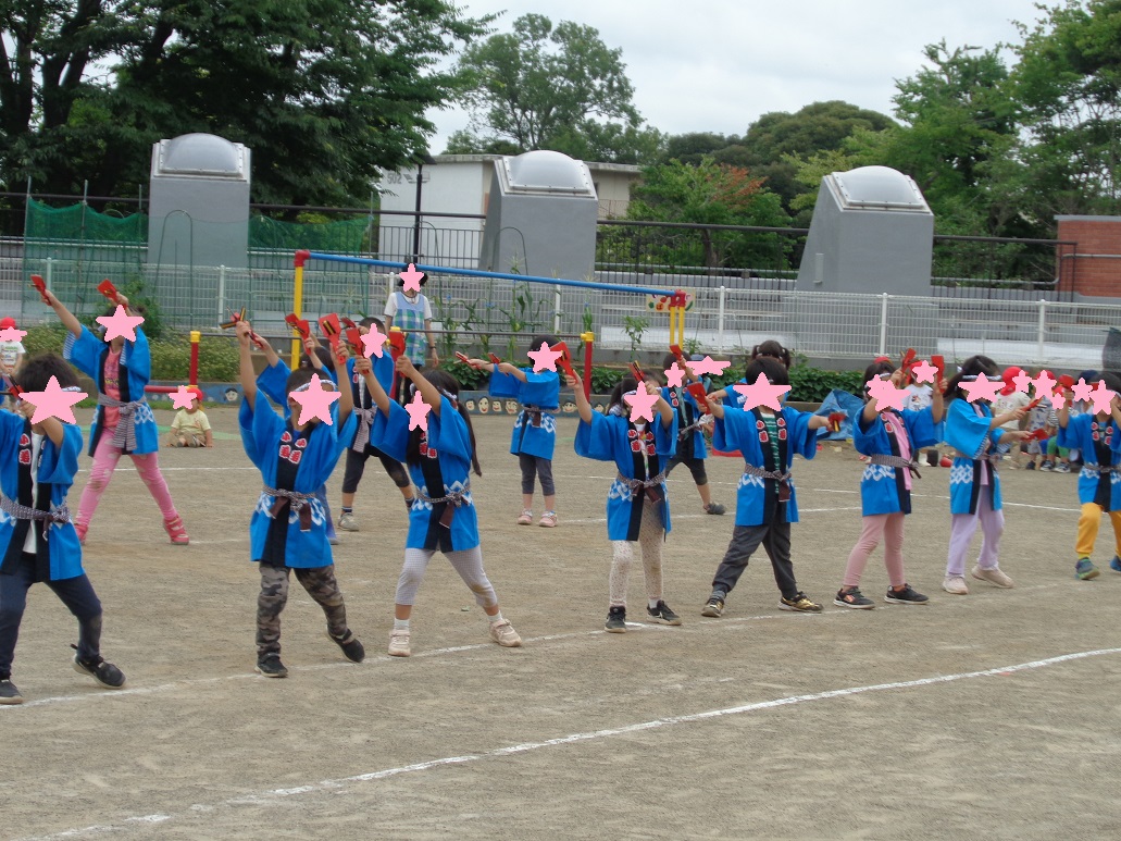 青色の法被を着て、両手に鳴子を持ち踊る子どもたち。