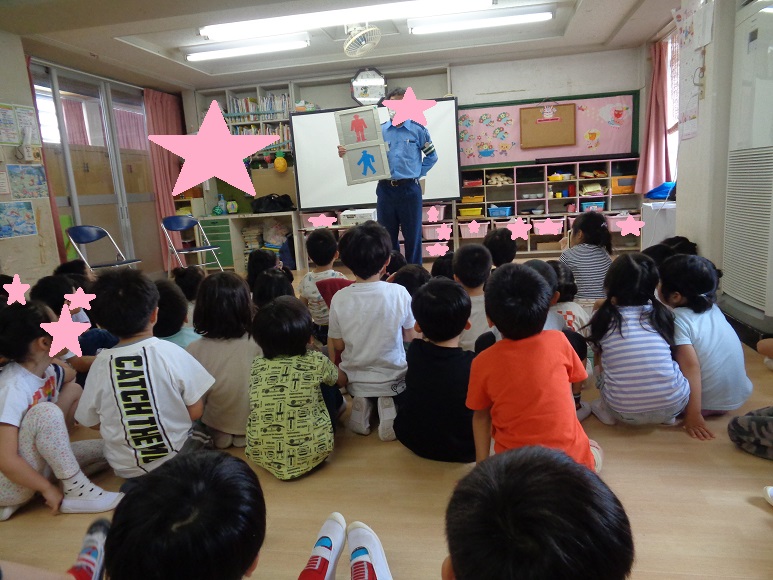 子どもたちが座って横断歩道の赤と青の信号標識を持った人の話を聞いている